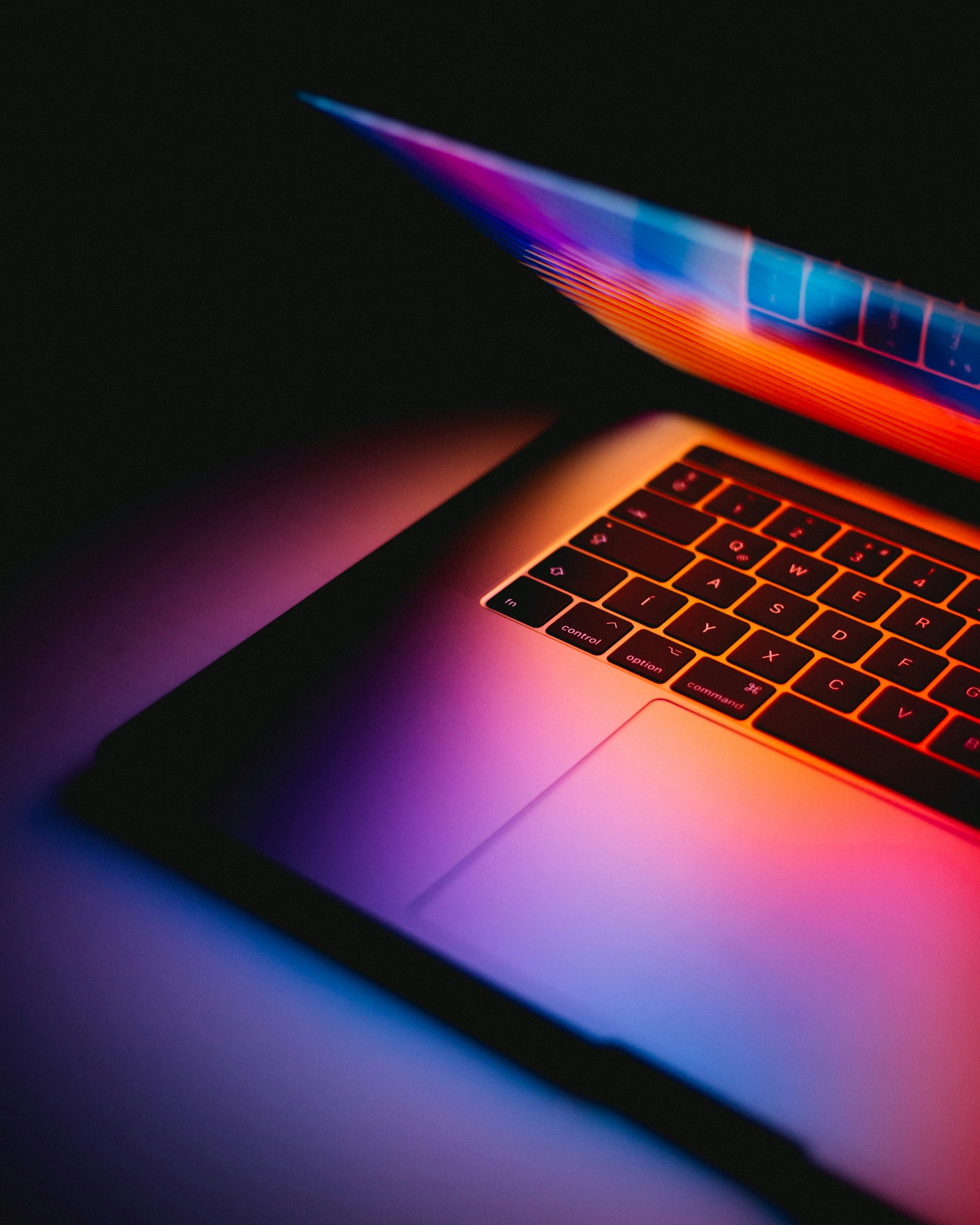 A macbook pro half open with a lot of colours on the screen reflecting on the keyboard.