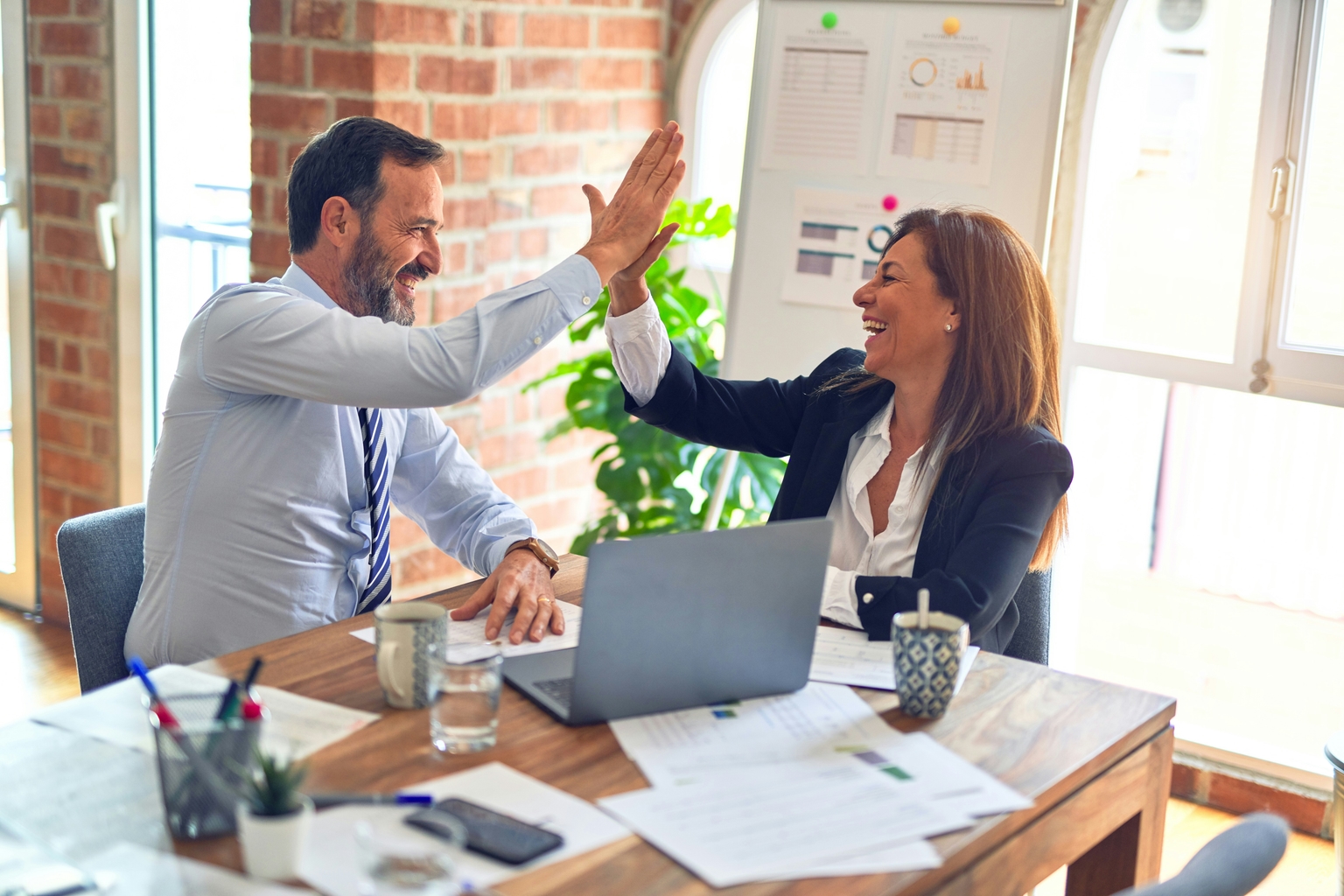 Two corporate people high fiving each other in front of a laptop.