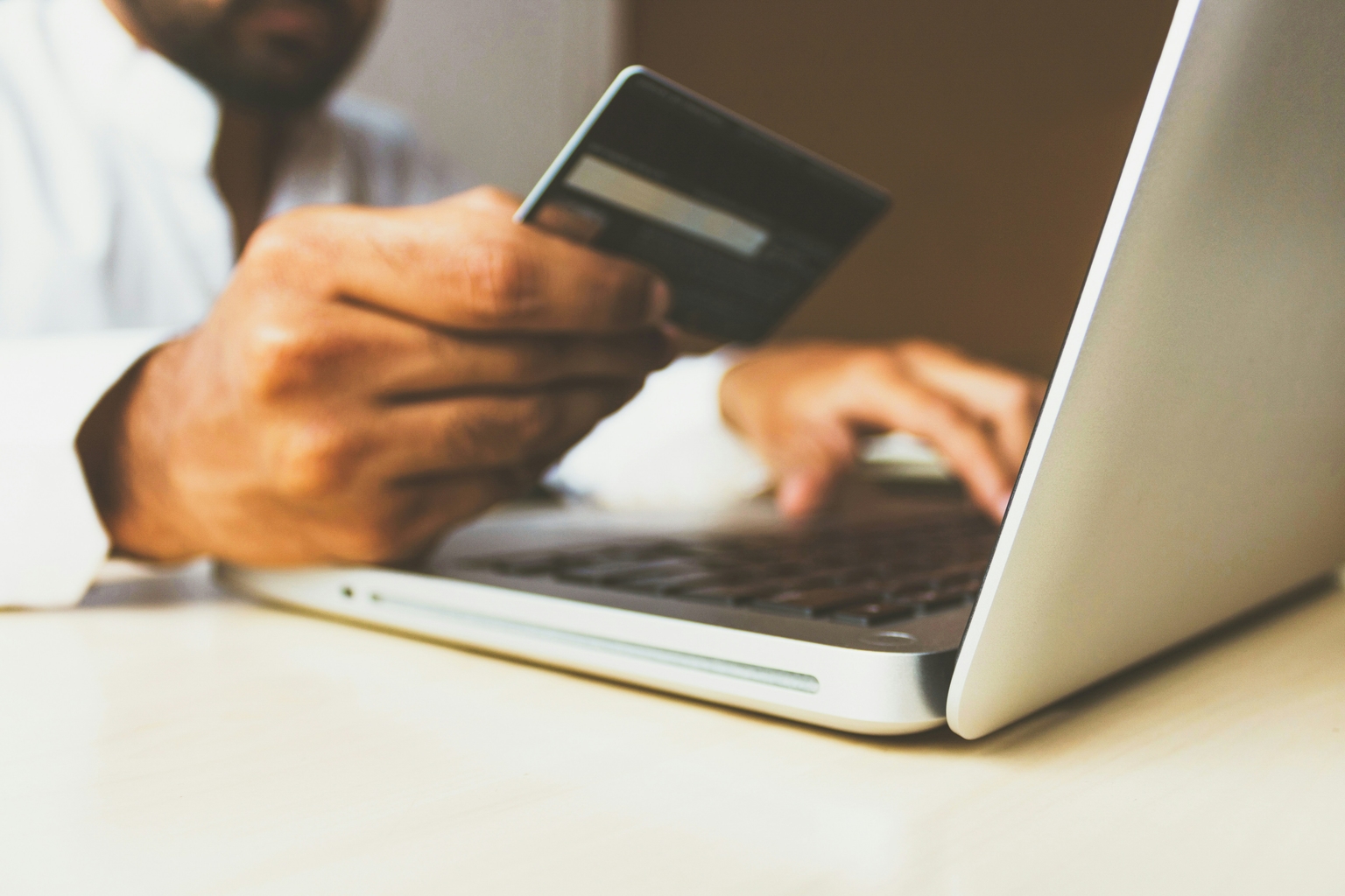 A person sitting in front of a computer with a credit card in the right hand and typing the numbers on the commputer with the other.