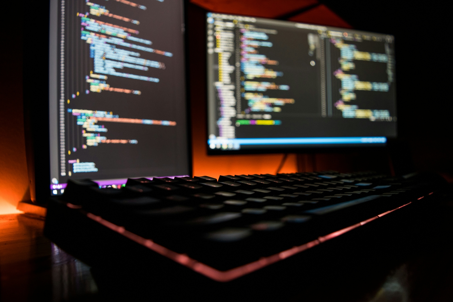 A keyboard and in the background two monitors with code.